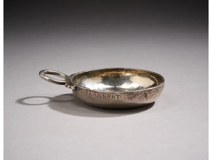Une tasse à vin en argent à décor uni, la prise en serpent, la bordure gravée L Lanbert.