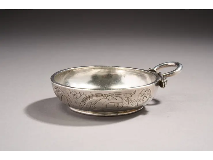 Tasse à vin en argent reposant sur une petite bâte.
